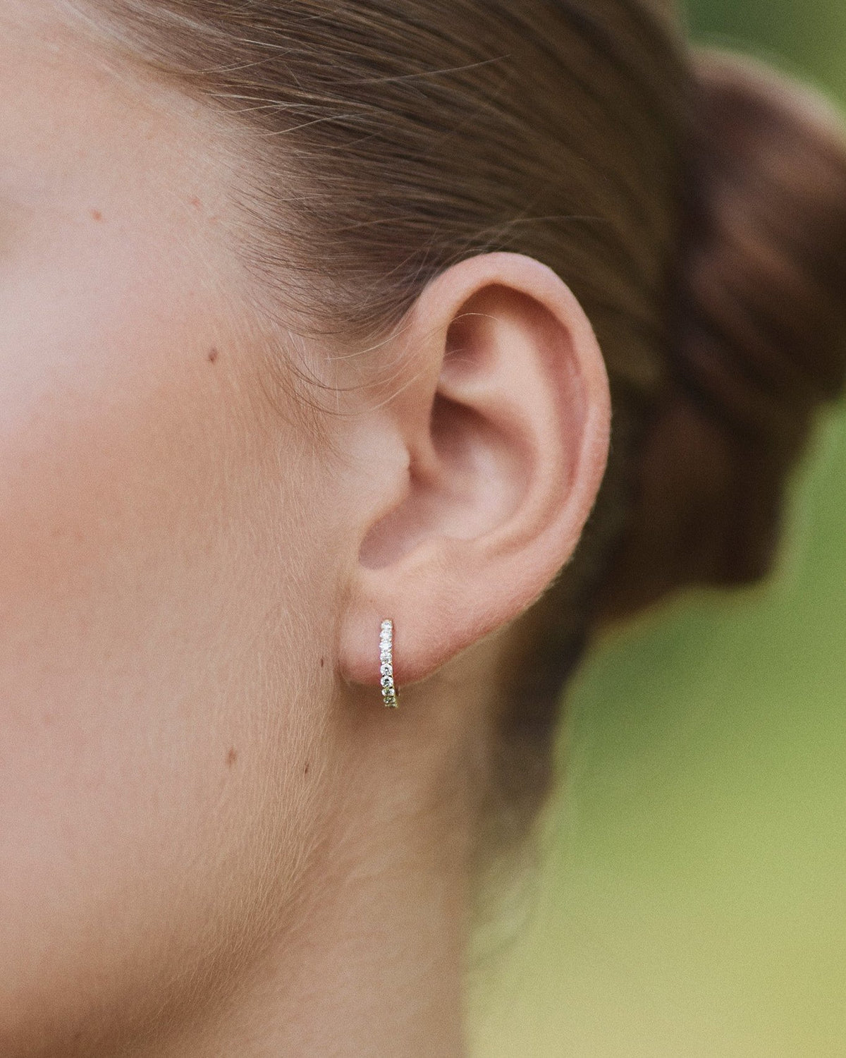 Close-up of an ear wearing a single Small Diamond Hoop earring in recycled 14K gold, set with 9 lab-grown diamonds in a click-closure design.