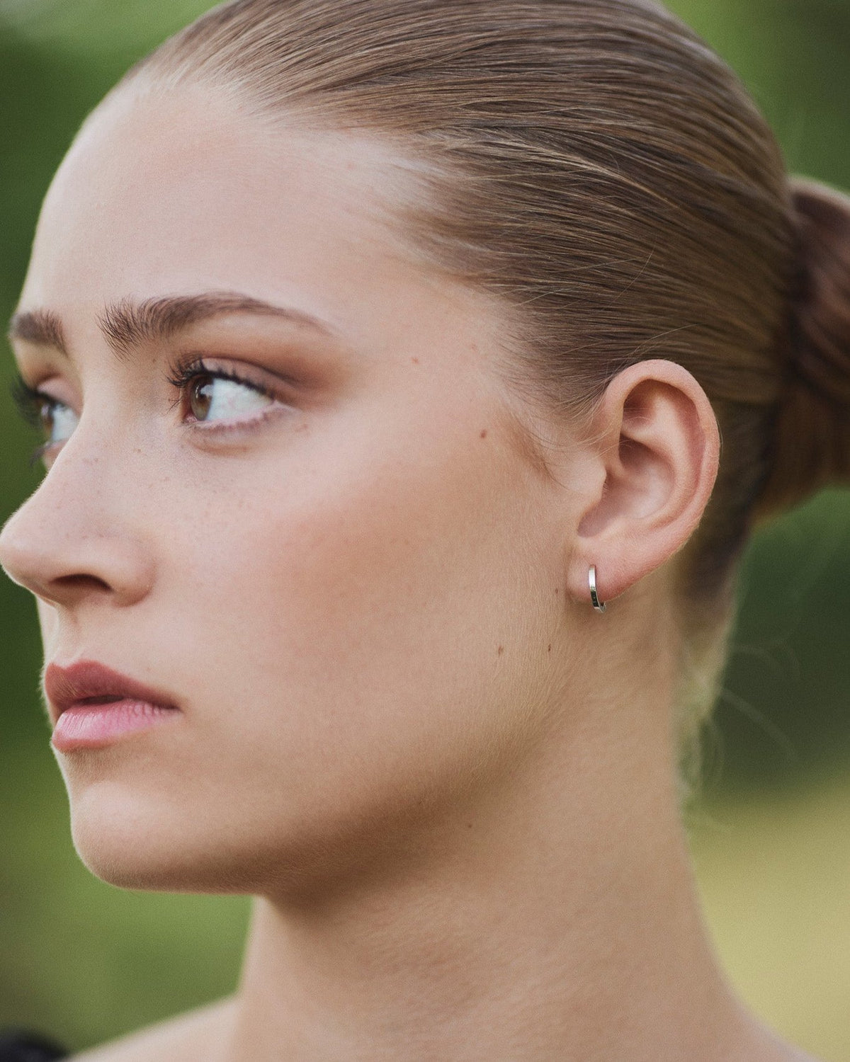 Model wearing a single Small Hoop earring in recycled 14K white gold with a click-closure design.
