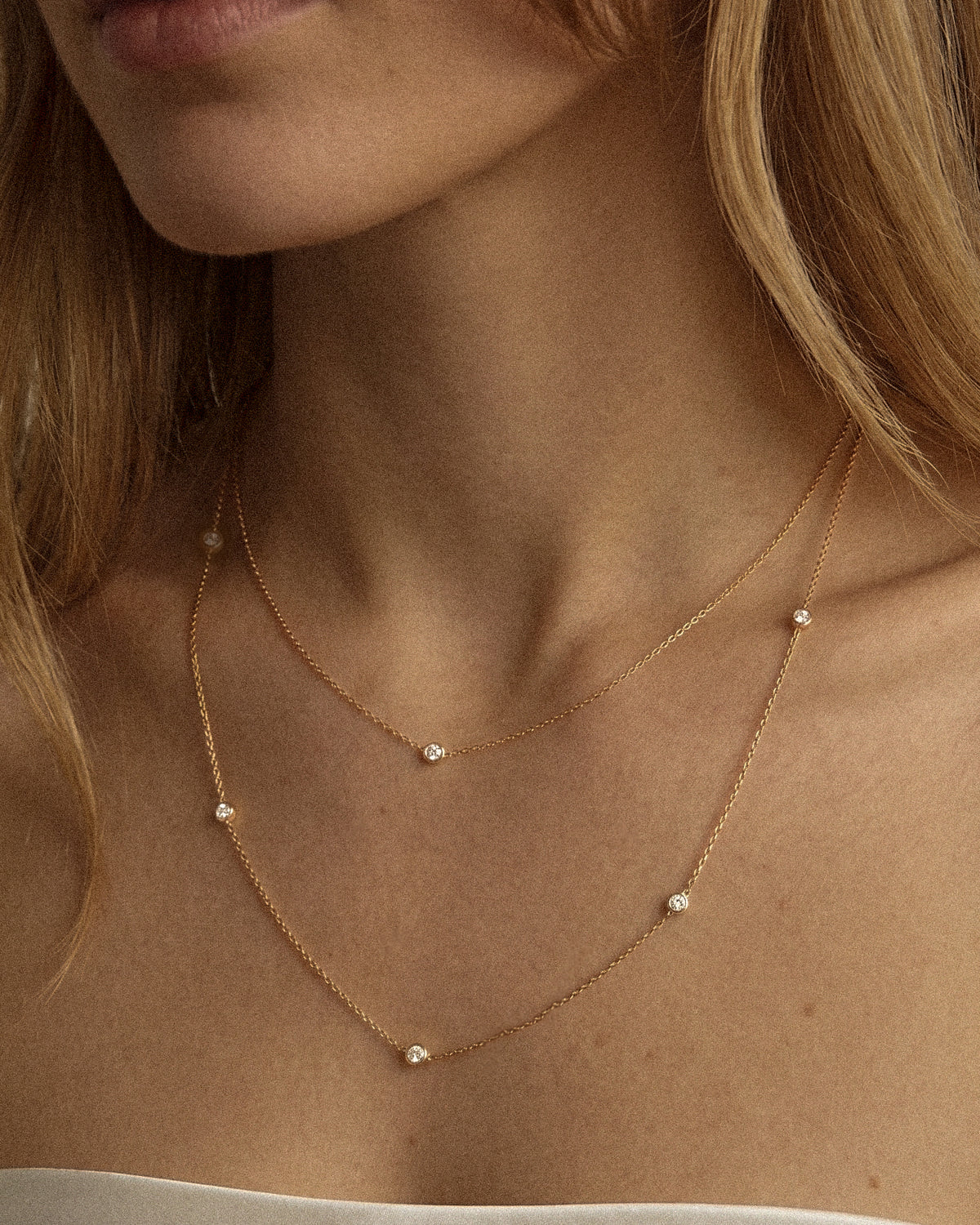The Bezel Diamond Necklace family in recycled 18K gold, worn layered at the neckline.