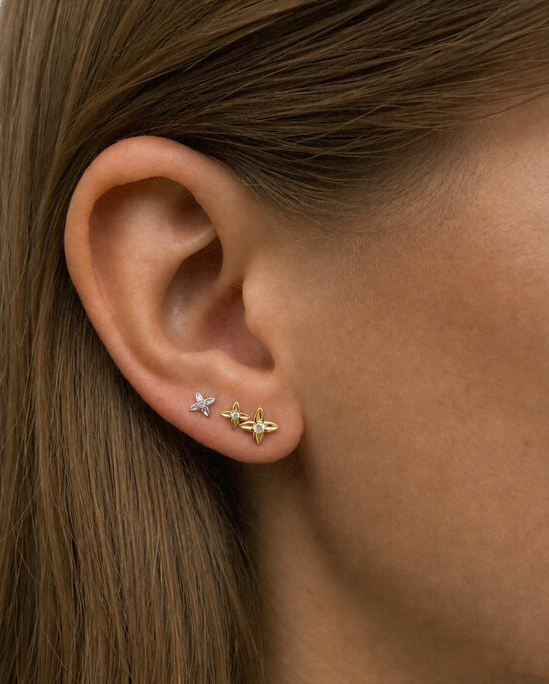 The Flora Stud earring in solid 14K gold, shown on the ear stacked with hoops.