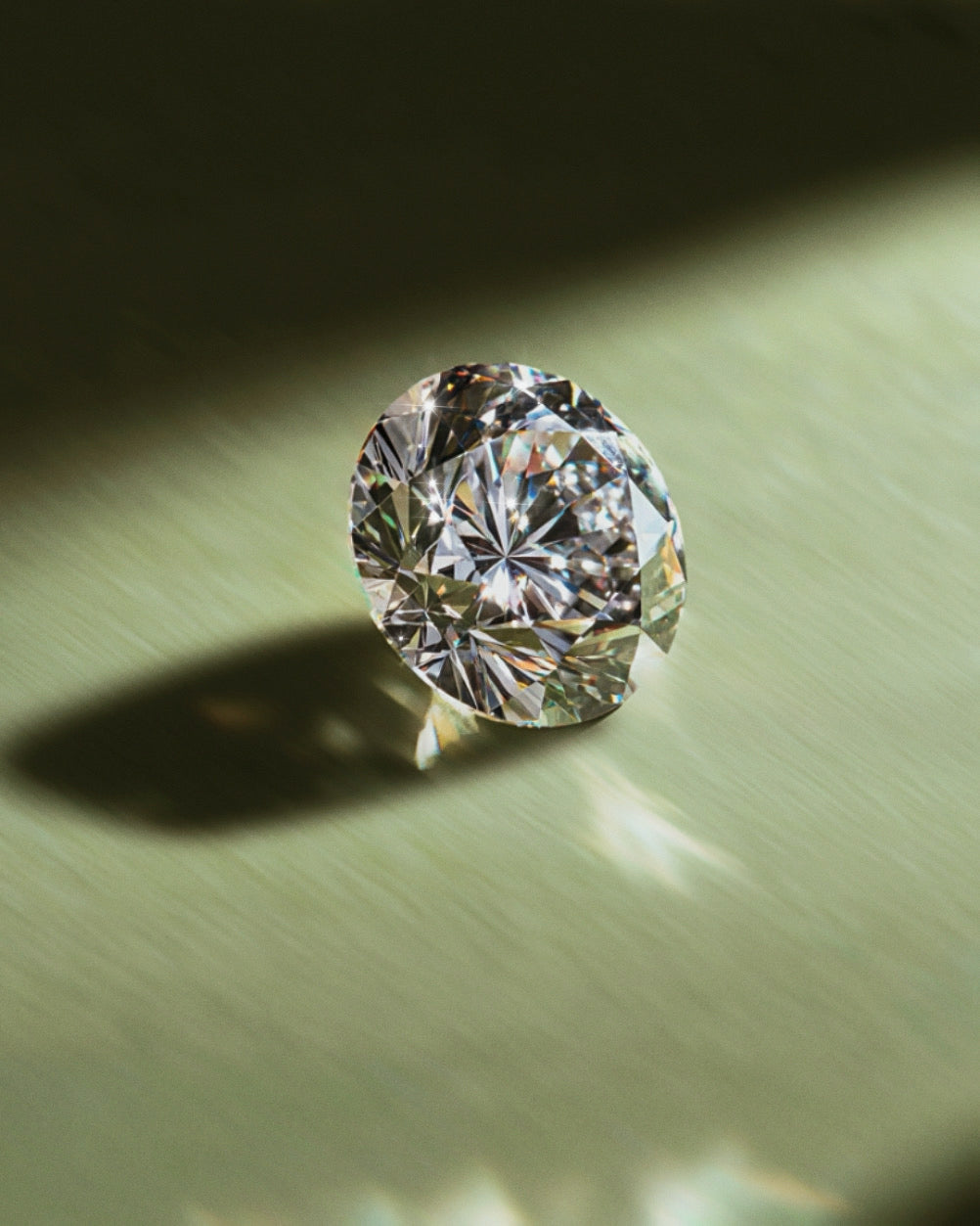 A sparkling round-cut diamond placed on a green surface, reflecting light and creating colorful prismatic highlights
