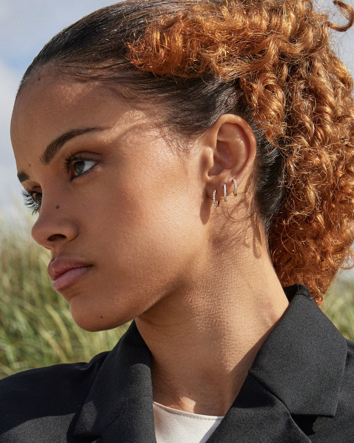 Model wearing three stacked Small Diamond Hoop earrings in recycled 14K gold, each set with 9 lab-grown diamonds in a click-closure design.