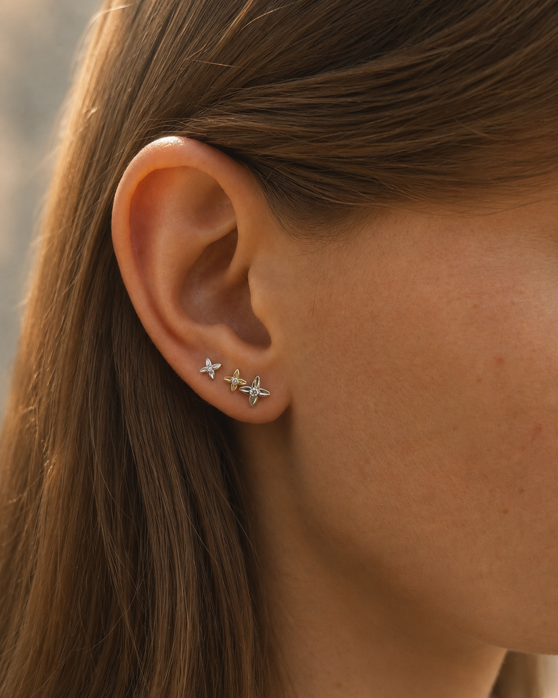 The Flora Stud earring in solid 14K white gold, shown on the ear stacked with hoops.