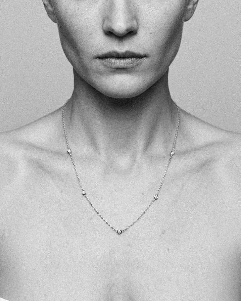 The Bezel Diamond Station Necklace in recycled 18K white gold, worn at the neckline.